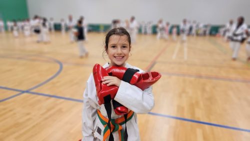 A young student smiling and holding kick pads at the club's August 2026 clinic