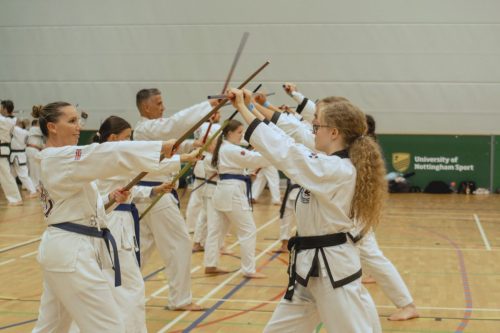 Students performing a bo staff technique in formation at the August 2026 GBTSDA clinic