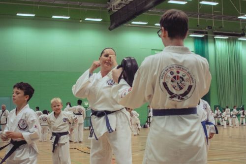 A student practising a strike on a focus pad while others watch at the August 2026 GBTSDA clinic