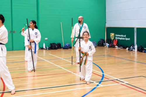 Students holding bo staffs in a line during the weapons session at the August 2026 GBTSDA clinic
