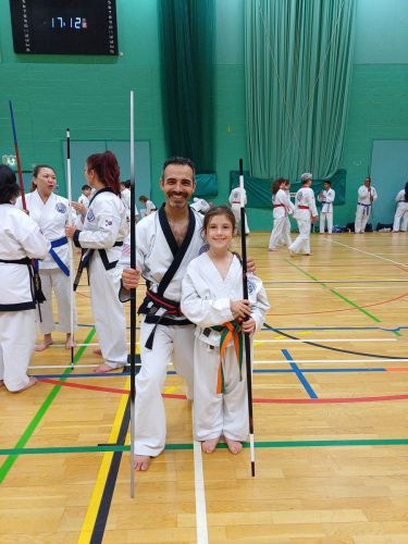 A black belt instructor posing with a young student and their bo staffs at the August 2026 GBTSDA clinic